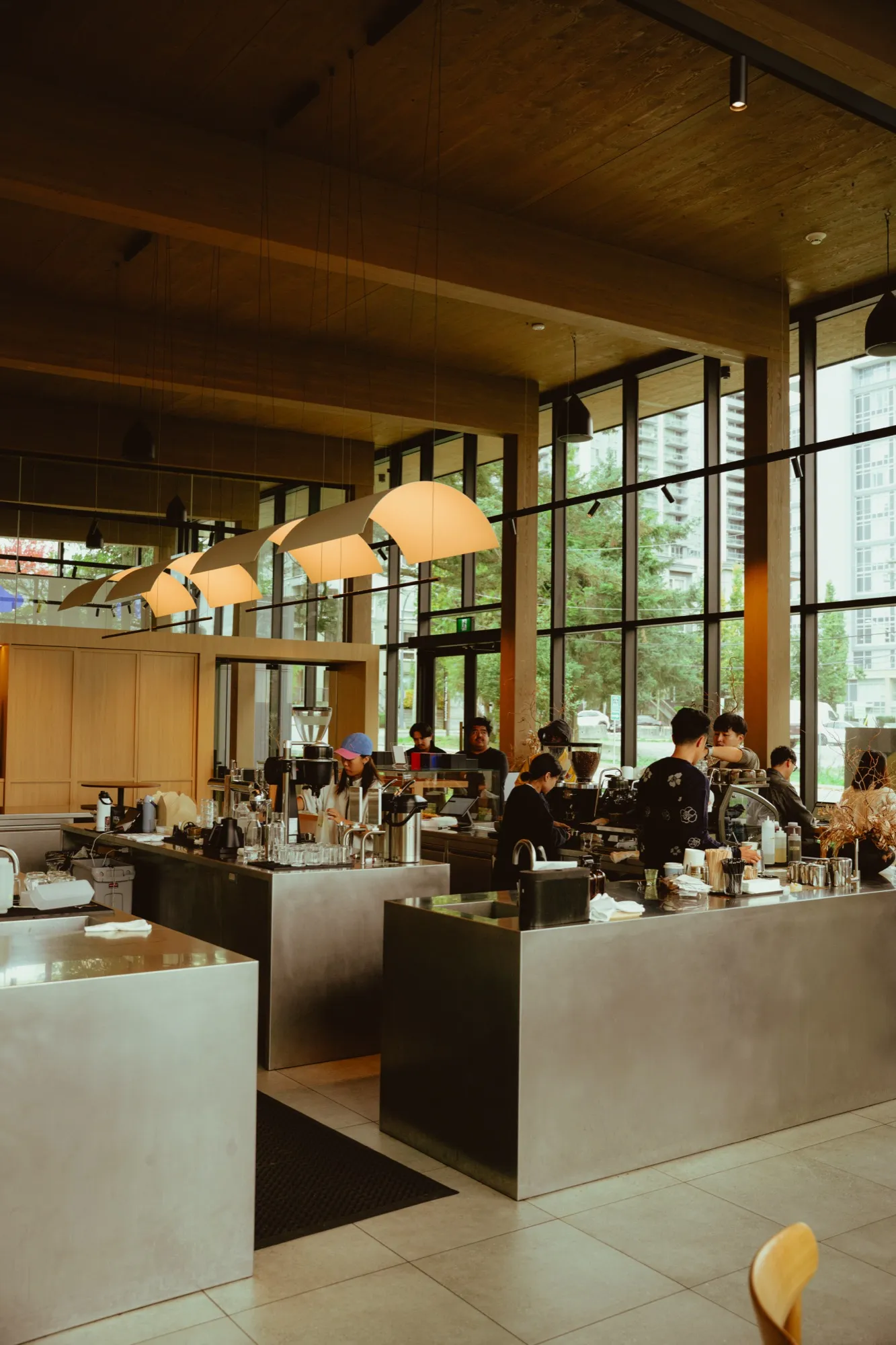 Modern cafe bar counter with baristas and dome pendant lights against floor-to-ceiling windows