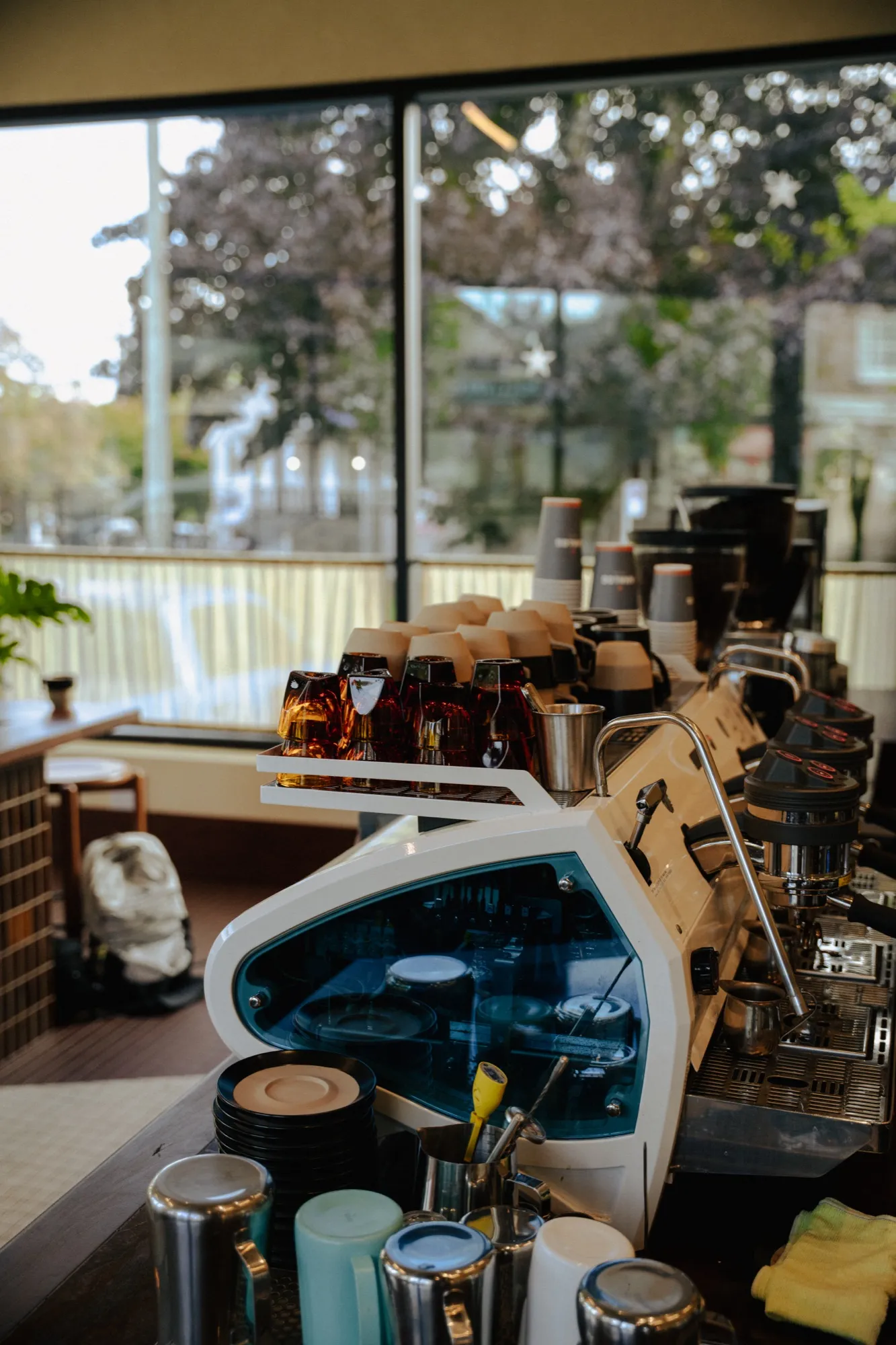 Vintage espresso machine with cups and cherry blossom trees visible through cafe window