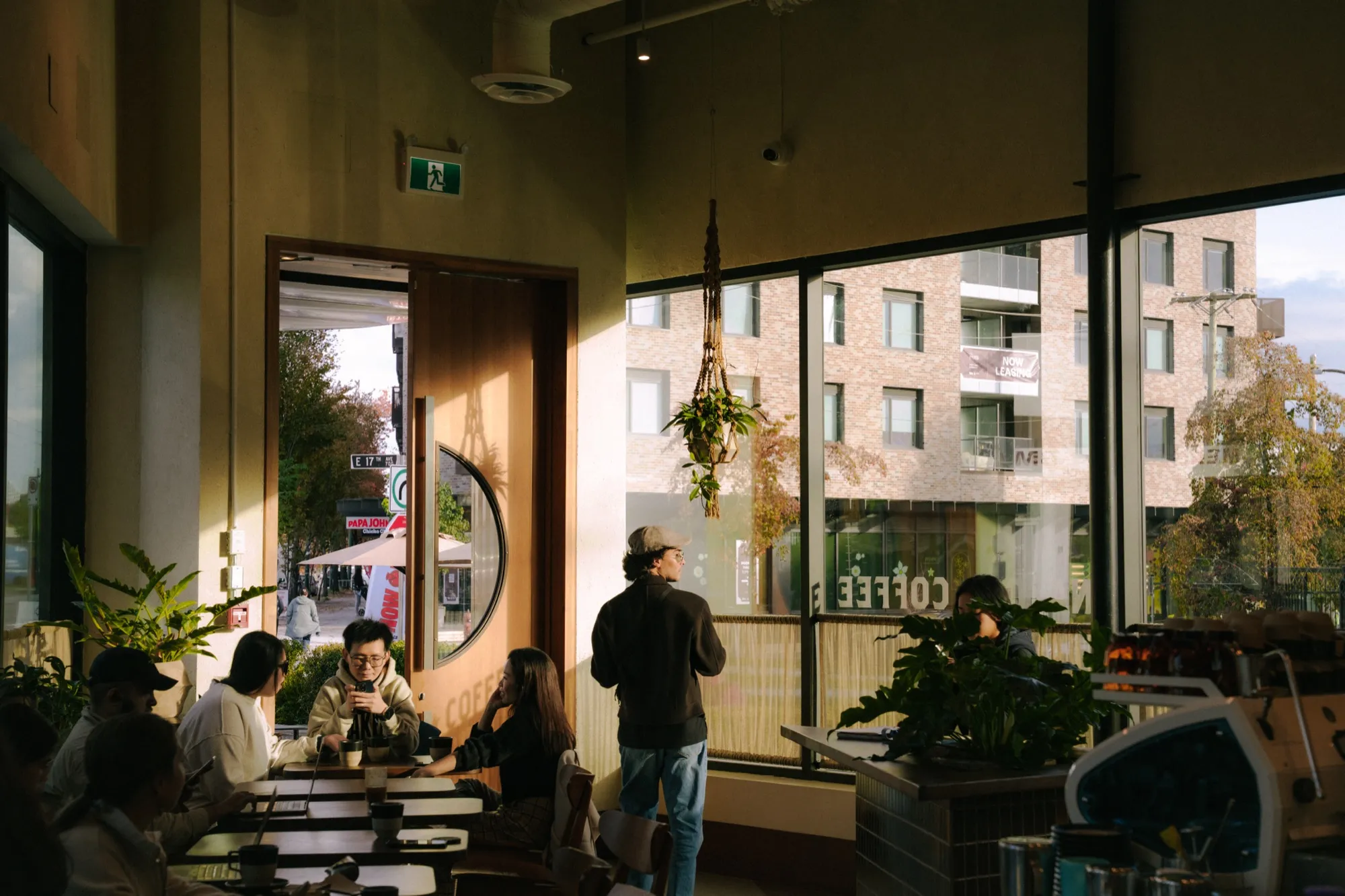 Golden hour cafe interior with people socializing near round window and hanging plants