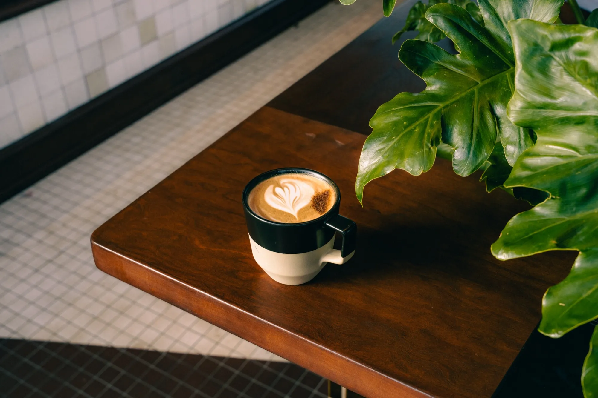 Latte art coffee on minimalist wooden cafe table with tropical plant and natural light